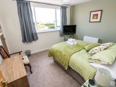 A bedroom with a bed with green bedding a wooden chair a wooden dresser and a television at 53 St Brides View in Roch