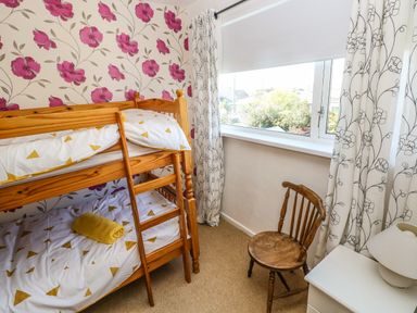A bedroom with wooden bunk beds a chair and a window with white floral curtains at 53 St Brides View in Roch