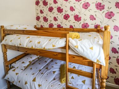A wooden bunk bed with white bedding and yellow triangle patterns and yellow towels in a room with floral wallpaper at 53 St Brides View in Roch