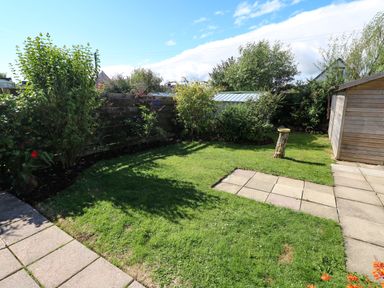 A garden with grass bushes a wooden shed a paved pathway and a tree stump at 53 St Brides View in Roch