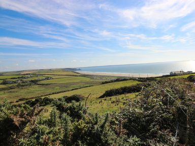 A coastal landscape with green fields and houses near a beach at 53 St Brides View in Roch