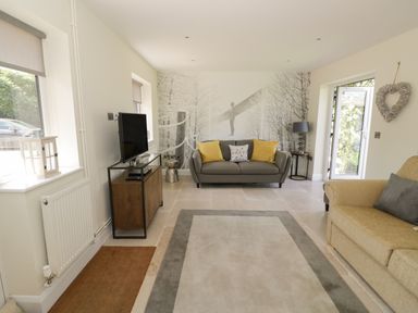 A living room with two sofas a television on a stand and a wall mural at Garden Cottage in Upton Upon Severn
