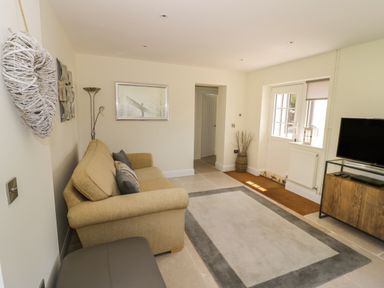 A living room with a beige sofa a floor lamp a wall mirror a flat screen TV on a wooden stand and a large rug at Garden Cottage in Upton Upon Severn