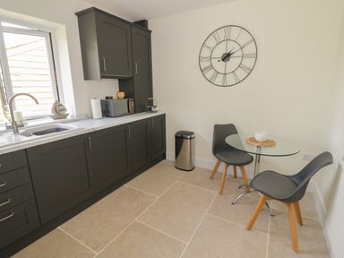 A kitchen with dark cabinets a sink and countertop and a small dining area with two chairs and a glass table at Garden Cottage in Upton Upon Severn