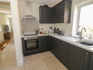 A kitchen with dark cabinets an oven a sink and appliances at Garden Cottage in Upton Upon Severn