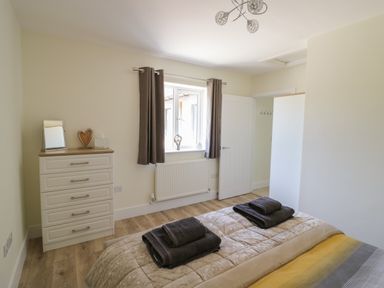 A bedroom with a bed, folded towels on the bed, a chest of drawers, and a window with curtains at Garden Cottage in Upton Upon Severn
