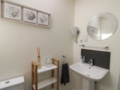 A bathroom with a white sink and toilet a wooden shelf with glass jars and a round mirror on the wall at Garden Cottage in Upton Upon Severn