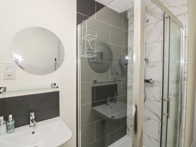A bathroom with a round mirror above a sink and a glass shower enclosure at Garden Cottage in Upton Upon Severn