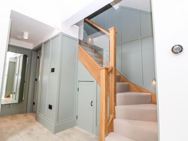 A staircase with wooden handrails and glass panels next to a wall with paneled doors at 12 Manor Farm Close in Kingham