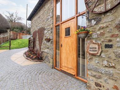 Stone building exterior with wooden door flower baskets and cobblestone path at Bagtor Granary in Ilsington