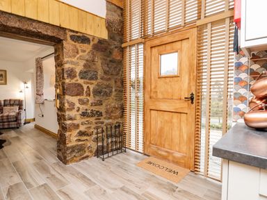 A wooden door with window and welcome mat near a stone wall and kitchen countertop at Bagtor Granary in Ilsington
