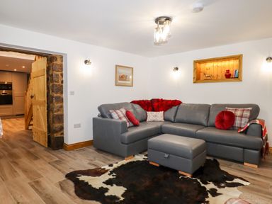 A living room with a gray sectional sofa red cushions and a cowhide rug at Bagtor Granary in Ilsington