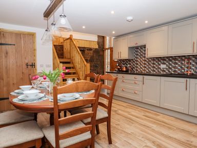 A kitchen and dining area with a wooden table set for four and a staircase in the background at Bagtor Granary in Ilsington
