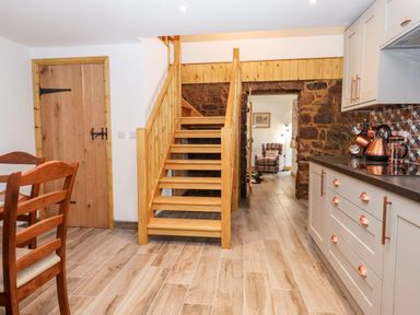A kitchen with wooden stairs and a dining table next to a wooden door at Bagtor Granary in Ilsington