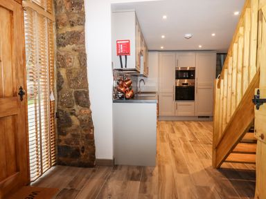 A kitchen with grey cabinets copper pots a wooden staircase and a wooden door with blinds at Bagtor Granary in Ilsington