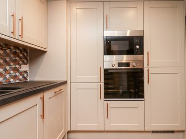 A kitchen with cream cabinets built in oven microwave and a tiled backsplash at Bagtor Granary in Ilsington