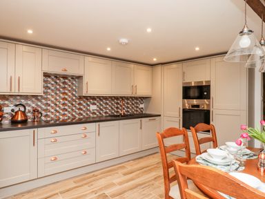 A kitchen with cabinets a patterned tiled backsplash and a dining table with chairs and tableware at Bagtor Granary Ilsington