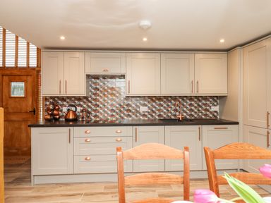 A kitchen with cabinets drawers and a countertop with copper utensils and a patterned tile backsplash at Bagtor Granary in Ilsington
