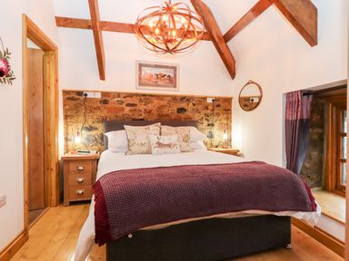 A bedroom with a double bed wooden beams and a window at Bagtor Granary in Ilsington
