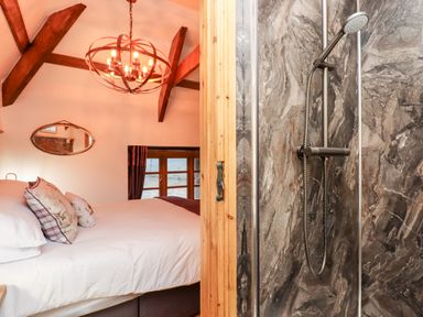 A bedroom with a bed and pillows next to a shower with marble walls at Bagtor Granary in Ilsington