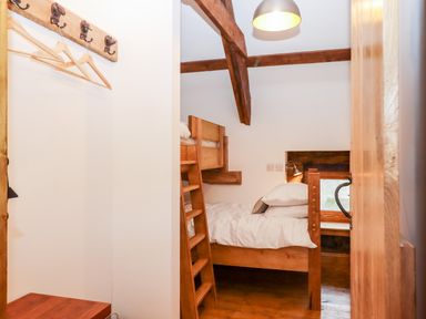 A small bedroom with wooden bunk beds a hanging rack with hangers and exposed wooden beams at Bagtor Granary in Ilsington