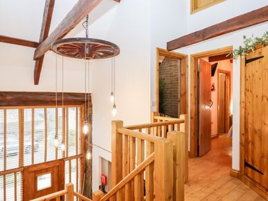 A wooden staircase with hanging light bulbs and doorways leading to rooms at Bagtor Granary in Ilsington