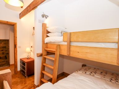 A bedroom with wooden bunk beds a small chest of drawers with a lamp and a wooden door frame at Bagtor Granary in Ilsington
