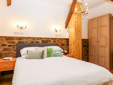A bedroom with a bed a wooden wardrobe stone wall and wooden beams at Bagtor Granary in Ilsington