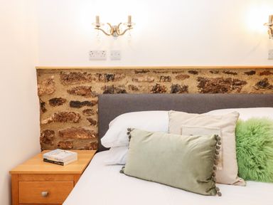 A bed with three pillows and a wooden bedside table with two books at Bagtor Granary in Ilsington