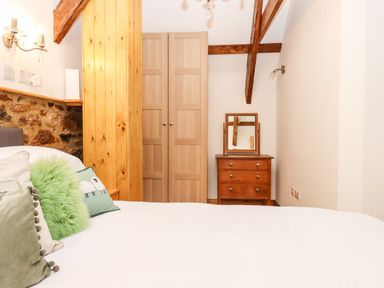 A bedroom with a bed pillows a wooden wardrobe and a dresser with a mirror at Bagtor Granary in Ilsington