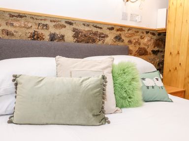A bed with four decorative pillows against a stone wall at Bagtor Granary in Ilsington