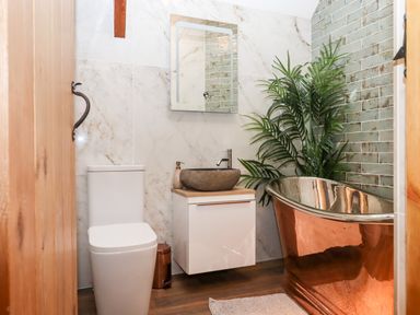 A bathroom with a toilet stone sink copper bathtub and plant at Bagtor Granary Ilsington