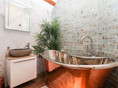 A bathroom with a copper bathtub a sink with a stone basin a mirror and a plant at Bagtor Granary in Ilsington