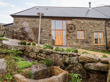 A stone building with wooden doors and windows near a small stream at Bagtor Granary in Ilsington