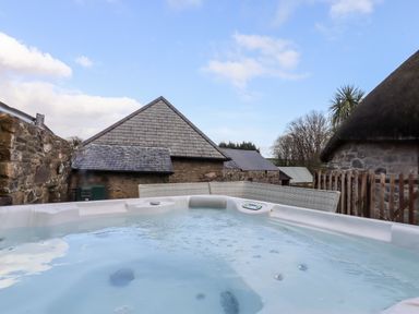 An outdoor hot tub with buildings and a wooden fence in the background at Bagtor Granary in Ilsington