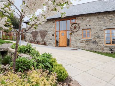 A stone building with wooden windows and door with a paved driveway and flowering tree in front at Bagtor Granary in Ilsington