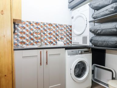 A laundry room with a washing machine and dryer stacked near a sink with a patterned tile backsplash at Bagtor Granary in Ilsington