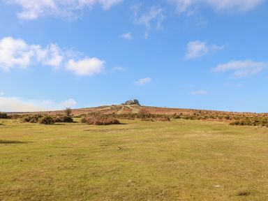An open grassy field with shrubs and a rocky hill under a blue sky at Bagtor Granary in Ilsington