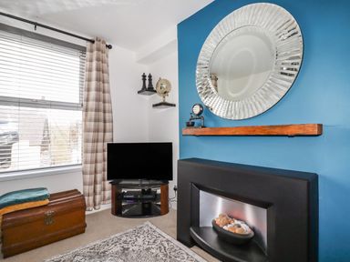 A living room corner with a television on a stand next to a window with curtains and a chest on the floor at Penmar in Looe