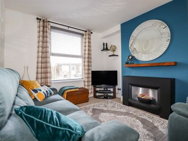 A living room with a blue sofa cushions a rug television and a fireplace at Penmar in Looe
