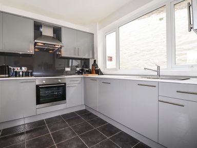 A kitchen with grey cabinets a black oven a stovetop a stainless steel hood and a large window at Penmar in Looe