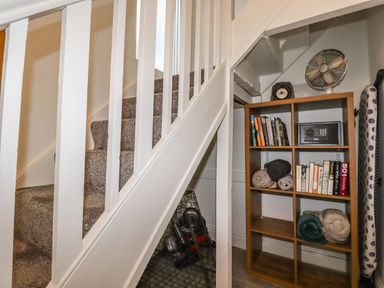 A carpeted staircase with a wooden shelving unit holding books blankets a fan and a safe at Penmar in Looe