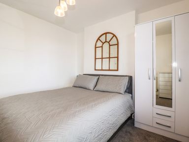 A bedroom with a bed covered in gray bedding a wall mirror with a wooden frame and a white wardrobe with a mirrored door at Penmar in Looe