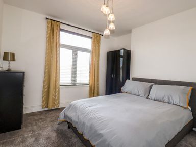 A bedroom with a double bed a black wardrobe a chest of drawers with a lamp yellow curtains and a window at Penmar in Looe