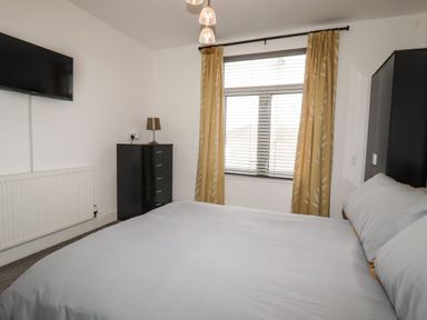 A bedroom with a bed a window with curtains a chest of drawers a lamp and a wall-mounted television at Penmar in Looe