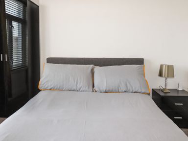 A bedroom with a bed with light gray bedding two pillows a nightstand with a lamp and a dark wardrobe at Penmar in Looe