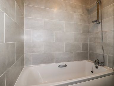 A bathroom with a bathtub and showerhead with tiled walls at Penmar in Looe