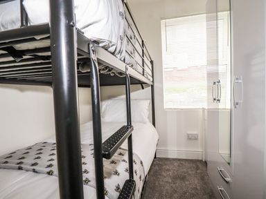 A small bedroom with a black metal bunk bed a window with blinds and a white wardrobe with a mirrored door at Penmar in Looe