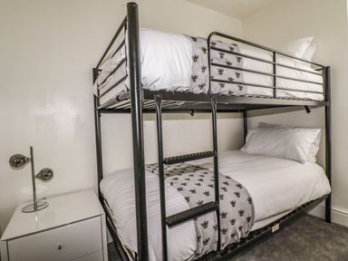 A bedroom with a metal bunk bed and a white bedside table with a lamp at Penmar in Looe