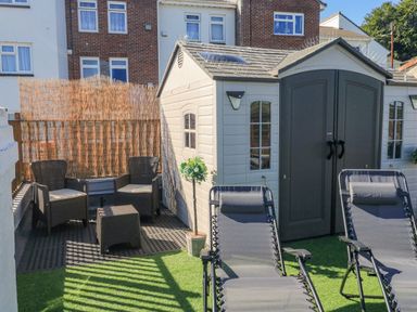 An outdoor patio with two lounge chairs, two armchairs, a small table, a potted plant, and a storage shed at Penmar in Looe